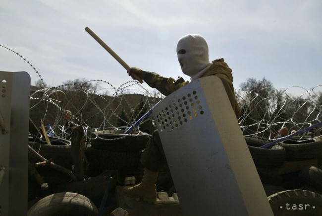 Maskovaný muž stojí na vrchole barikády pri budove oblastnej správy v v Donecku, Ukrajina, pondelok 7. apríla 2014