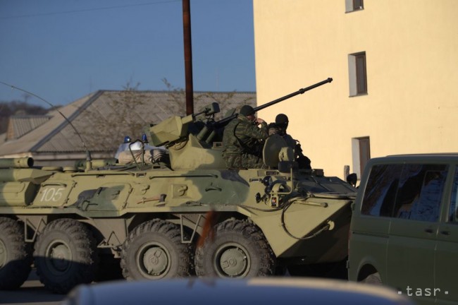Vojaci v neoznačených uniformách sedia na tanku pri bráne základne Beľbek neďaleko prístavu Sevastopol, Krym, sobota 22 marec 2014. 